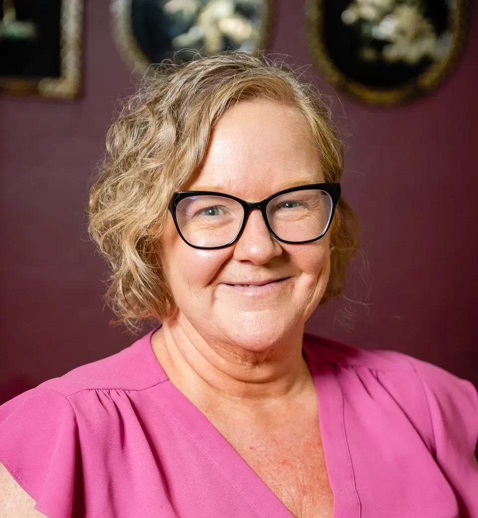 A woman in pink shirt and glasses smiling for the camera.