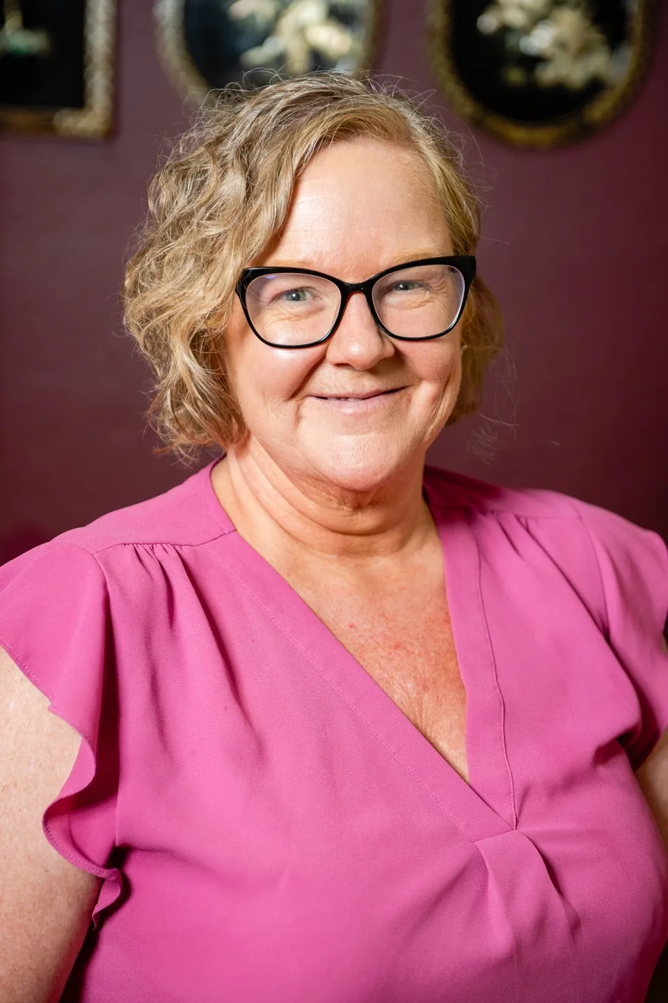 A woman in pink shirt and glasses smiling for the camera.